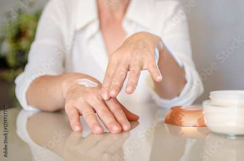 mulher branca de 50 anos massageando as mãos com creme hidratante
