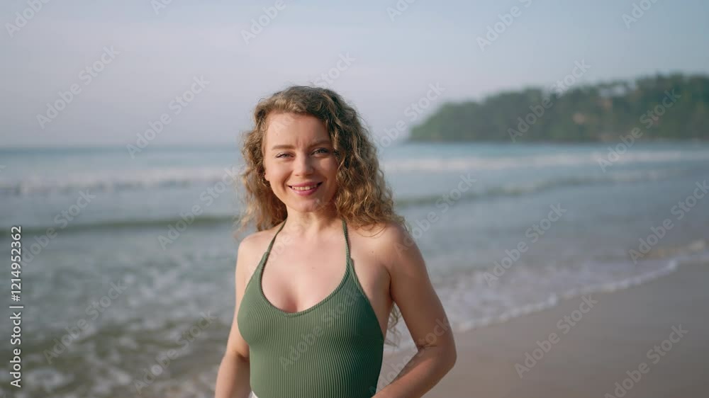 Curly-haired woman smiles, strolls along tropical shore. Casual beach walk in swimsuit, enjoying sun. Vacationer relaxes by sea, freedom. Tourist holds straw hat, breathes fresh ocean air. Curly-haired woman smiles, strolls along tropical shore. Casual beach walk in swimsuit, enjoying sun. Vacationer relaxes by sea, freedom. Tourist holds straw hat, breathes fresh ocean air.