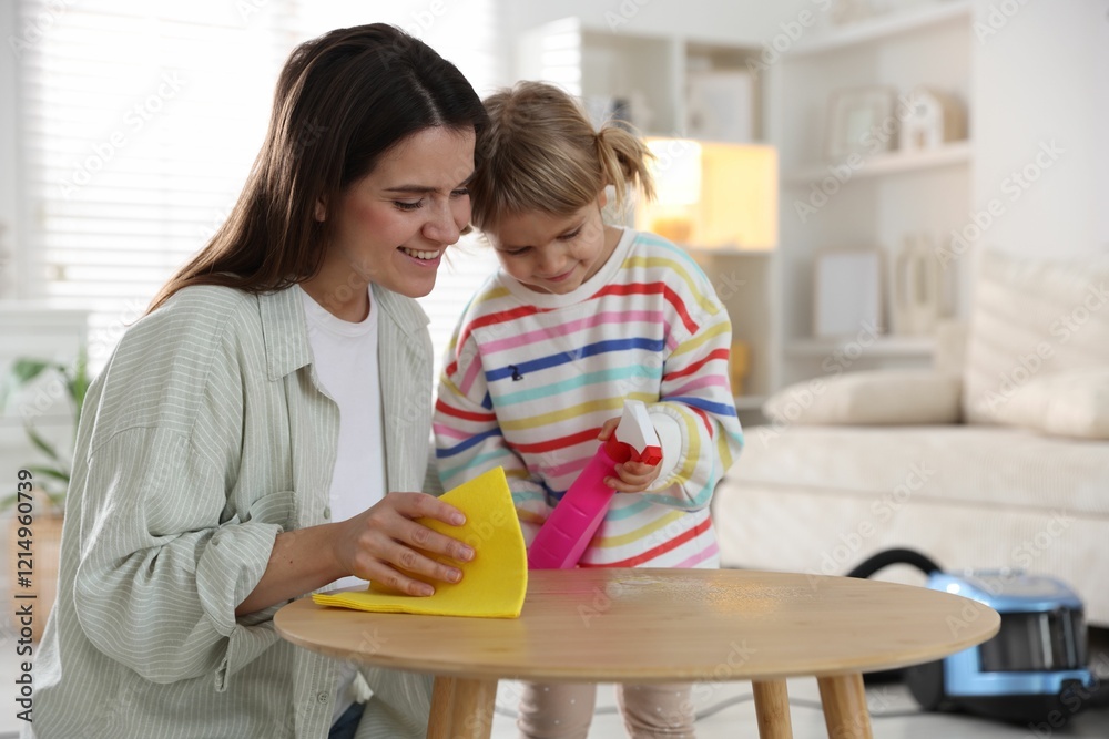 Cute little girl helping her mother wiping wooden table at home Cute little girl helping her mother wiping wooden table at home