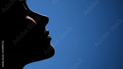 Silhouette of a Profile Against a Bright Blue Background Highlighting Facial Features and Expression in Soft Lighting Conditions photo