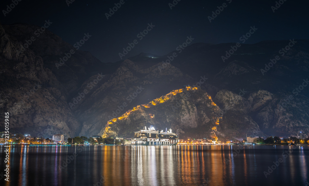 cruise ship on Kotor with fortress and mountains at night in Montenegro