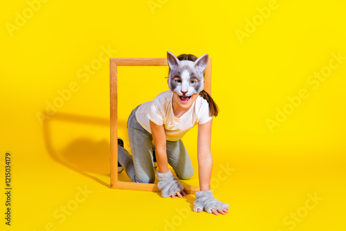 Young girl in casual outfit wearing a cat mask surrounded by a vibrant yellow background, presenting playfulness and creativity. photo