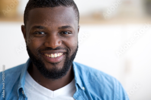 Closeup portrait of positive young African American guy sincerely smiling at camera, cheerful black millennial student guy in blue shirt, free space. High quality photo