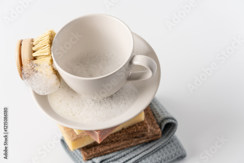 Stack of sponges, rags, natural soap and clean white cup with brush on white background. Eco-friendly dishwashing concept photo