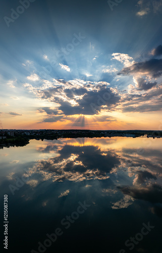 Obraz na płótnie A captivating landscape photo of a sunset casting radiant light beams through clouds, perfectly reflected in the calm lake below. Sunset reflection photo. w salonie