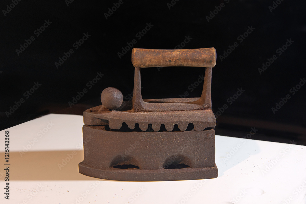 Cast iron iron on a black background. Antique coal iron. Antique household item.
Cast iron iron on a black background. Antique coal iron. Antique household item.