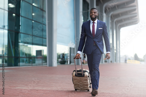 Portrait of young african american man walking in airport terminal with luggage, smiling african guy carrying suitcase while going to boarding gate, enjoying air travels and business trips, copy space