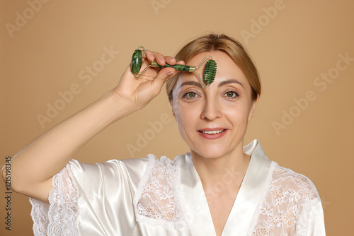 Smiling woman doing facial self massage with roller on beige background photo