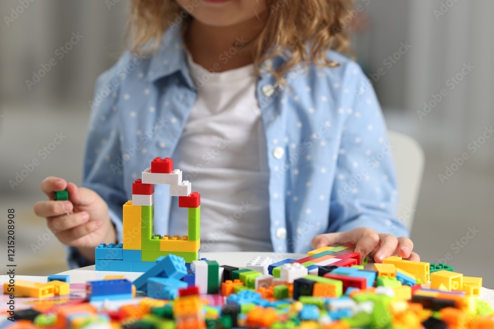 Fototapeta premium Girl playing with building blocks at white table indoors, closeup