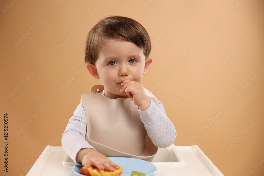Healthy baby food. Cute little kid eating fruits in high chair on beige background Healthy baby food. Cute little kid eating fruits in high chair on beige background