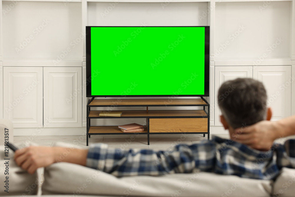 Fototapeta premium Man watching TV on sofa at home, back view