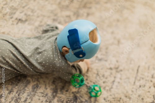 a baby boy wearing a blue Helmet for molding therapy, for cranial orthosis for plagiocephaly while laying on the carpet in his nursery room