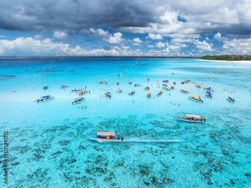 Fototapeta Naklejka Na Ścianę i Meble -  Aerial view of colorful boats in clear azure water in summer. Mnemba island, Zanzibar. Top drone view of sandbank in low tide, blue sea, white sand, swimming people, yachts, sky with clouds. Ocean