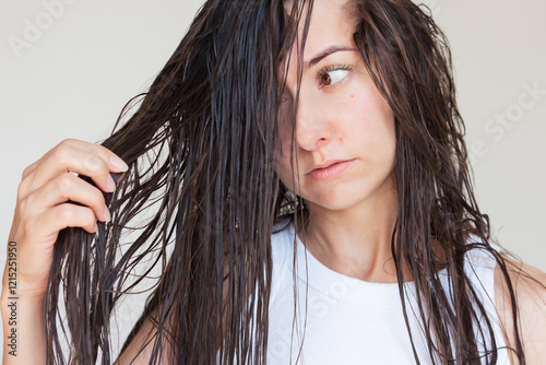A young Caucasian brunette woman looking at her long wet tangled hair after shampooing. Hair care