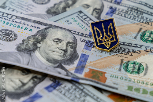 Hundred dollar bills are scattered on the table. The pin in the form of the Coat of arms of Ukraine lies on the dollars. The national emblem of Ukraine is a trident. Finance of the United States photo