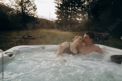 A young couple of a man and a woman are relaxing in a jacuzzi on a weekend, gently embracing. The background is a beautiful landscape of nature.