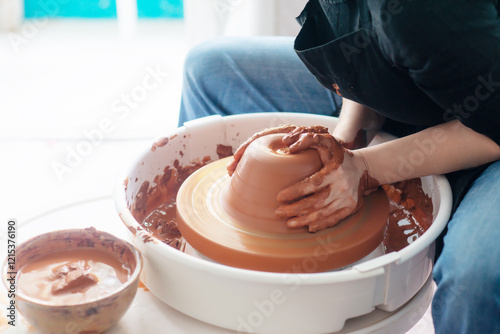 Female hands throwing a large sized bowl on a potter's wheel in a sunlit pottery studio photo