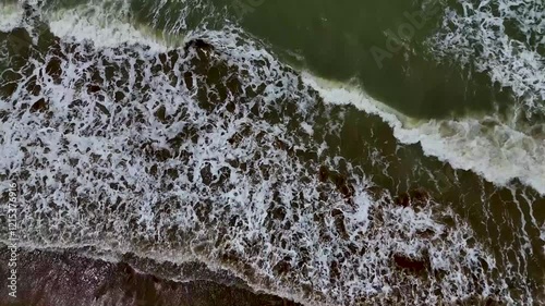 Static drone shot of the ocean with calm waves reaching the shore of a white sand beach on a tropical island of Pakistan during bright sunny day