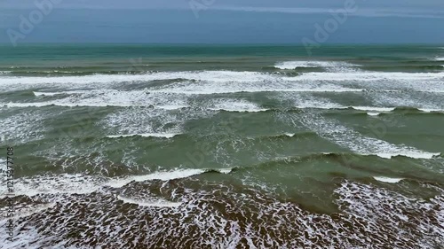 Static drone shot of the ocean with calm waves reaching the shore of a white sand beach on a tropical island of Pakistan during bright sunny day