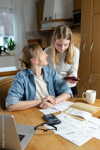Mom and daughter look at bills and papers together at the table, discussing financial issues. The scene illustrates family interaction, help, and learning to manage household expenses.