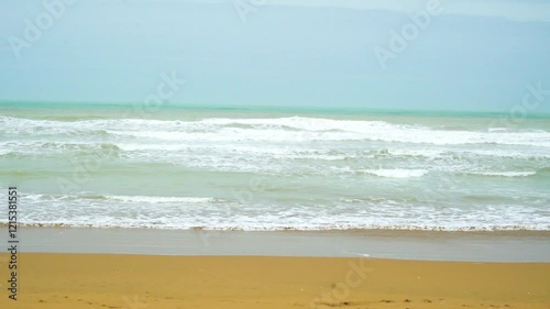 Static drone shot of the ocean with calm waves reaching the shore of a white sand beach on a tropical island of Pakistan during bright sunny day