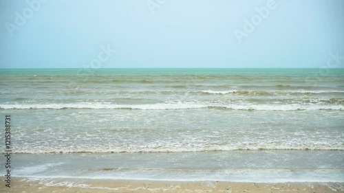 Static drone shot of the ocean with calm waves reaching the shore of a white sand beach on a tropical island of Pakistan during bright sunny day