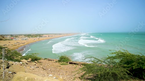 Static drone shot of the ocean with calm waves reaching the shore of a white sand beach on a tropical island of Pakistan during bright sunny day