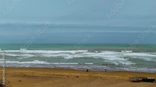Static drone shot of the ocean with calm waves reaching the shore of a white sand beach on a tropical island of Pakistan during bright sunny day