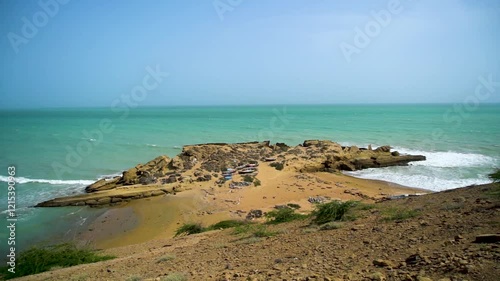 Static drone shot of the ocean with calm waves reaching the shore of a white sand beach on a tropical island of Pakistan during bright sunny day
