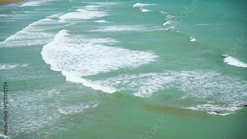 Static drone shot of the ocean with calm waves reaching the shore of a white sand beach on a tropical island of Pakistan during bright sunny day