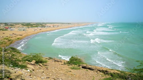 Static drone shot of the ocean with calm waves reaching the shore of a white sand beach on a tropical island of Pakistan during bright sunny day