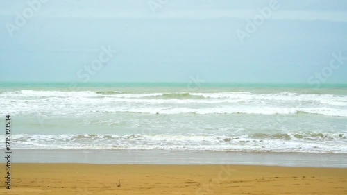 Static drone shot of the ocean with calm waves reaching the shore of a white sand beach on a tropical island of Pakistan during bright sunny day