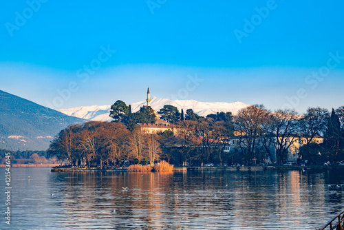 Ioannina lake in Greece with reflective waters and birds in sunset. Snow covered mountains in the backgorund and the minaret of Aslan Pasha Mosque.  photo