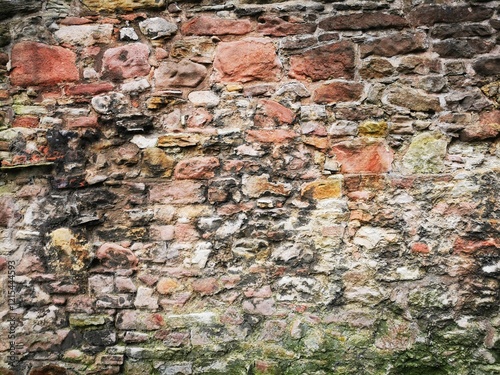 Background: Uneven old wall with different colored patched clinker bricks. Closeup. Walls of Edinburgh, Scotland, UK. Sandstone. Moss stains. Antique photo