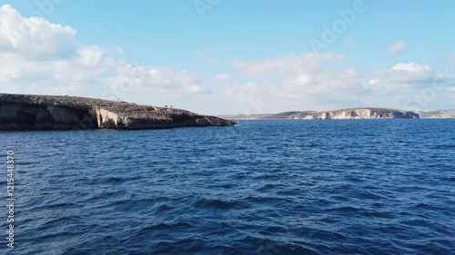 Rocky coast of the northern part of the island of Malta as seen from the sea, with the island of Comino in the background