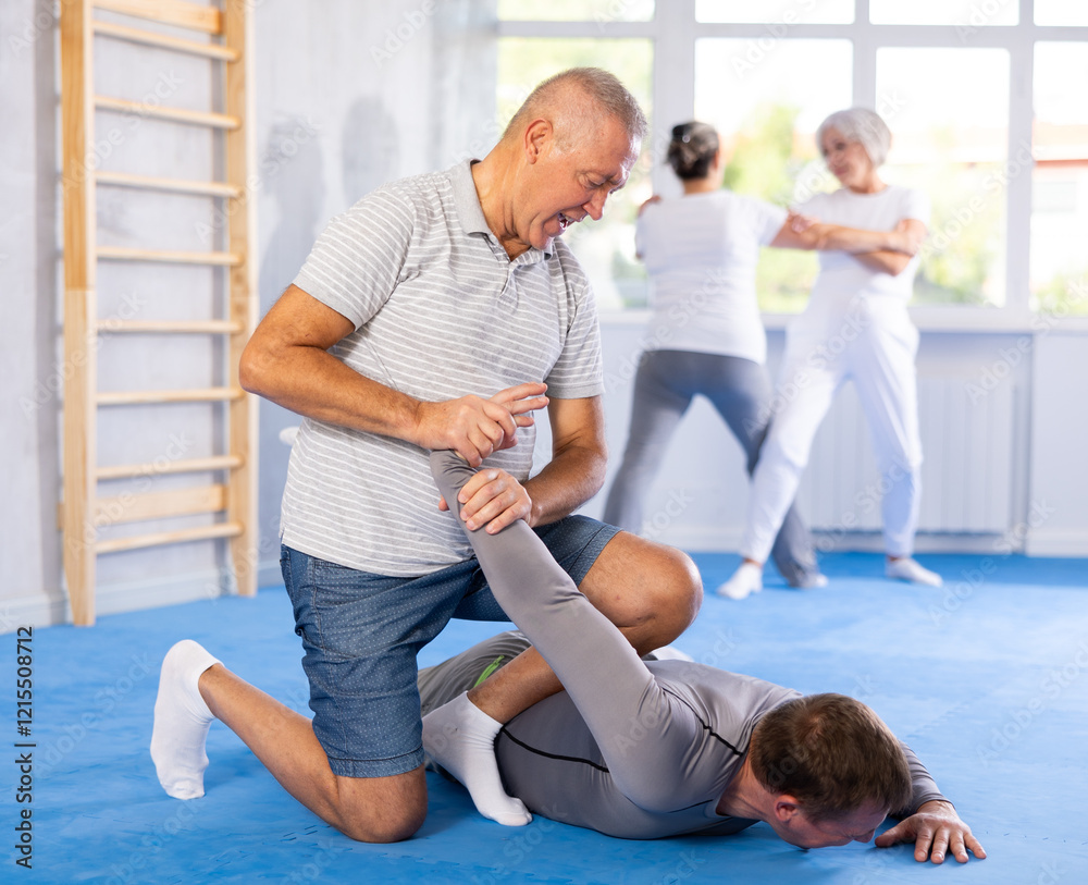 Obraz premium Self-defense lesson - elderly man twists the arm of attacking man with painful hold in gym