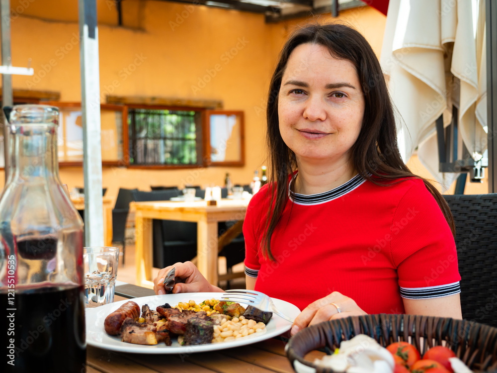 Portrait of woman spending time on open terrace of catalan restaurant and eating traditional parillada de carne Portrait of woman spending time on open terrace of catalan restaurant and eating traditional parillada de carne