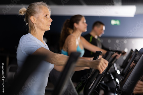 Elterly fitness woman in sportswear doing cardio training on ellipsoid in gym