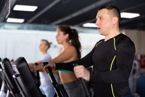 Middle-aged man in the gym is engaged in sports using an ellipsoid simulator. Healthy lifestyle and sport concept
