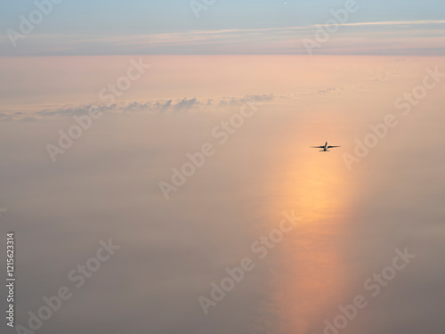 Airplane flies above white clouds and ocean water at dawn 