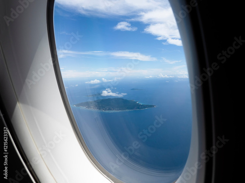 View through airplane window, porthole of an airplane that flying above the clouds and coast of one of Seychelles island La Digue
