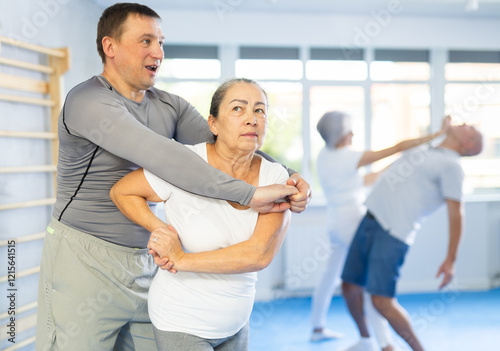 Senior woman train in pair with middle-aged coach to strike and reflect blows of enemy. Intense moment as two individuals engage in self-defense training, showcasing skill, reaction, repulse