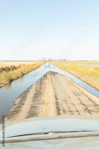 Vertical view of a remote American farm road with excess rain and sea water collecting upon the double yellow lined asphalt due to rising ocean levels combined with land erosion 