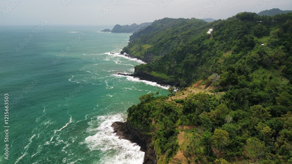 Fototapeta premium Aerial drone view of coastline with hills and trees, as well as view of coral cliffs and sea with waves from the ocean in Sagara view also known as Karang Bolong Beach Kebumen Central Java Indonesia