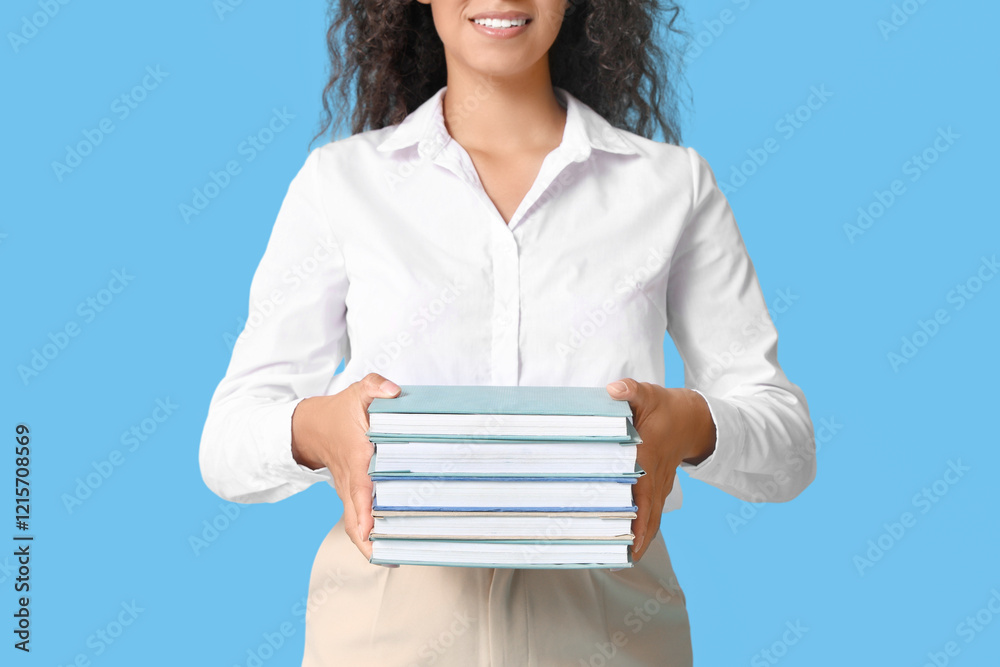 Young African-American woman with stack of books on blue background Young African-American woman with stack of books on blue background