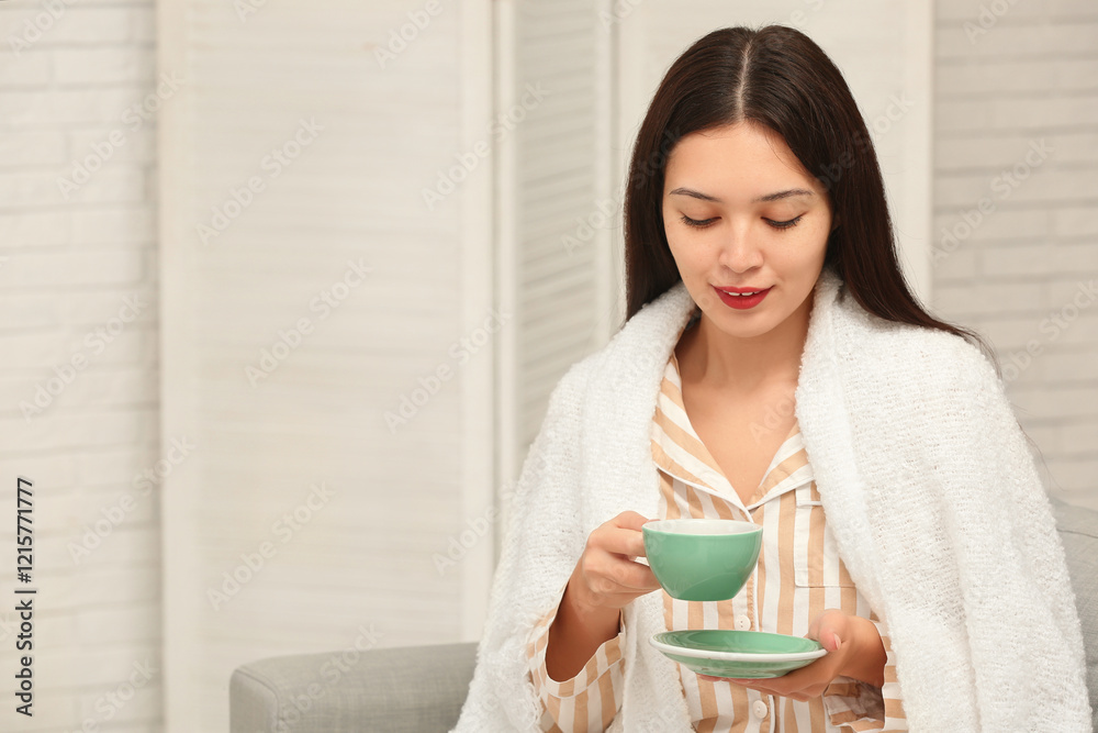Beautiful young Asian woman with cup of hot tea and saucer in living room Beautiful young Asian woman with cup of hot tea and saucer in living room