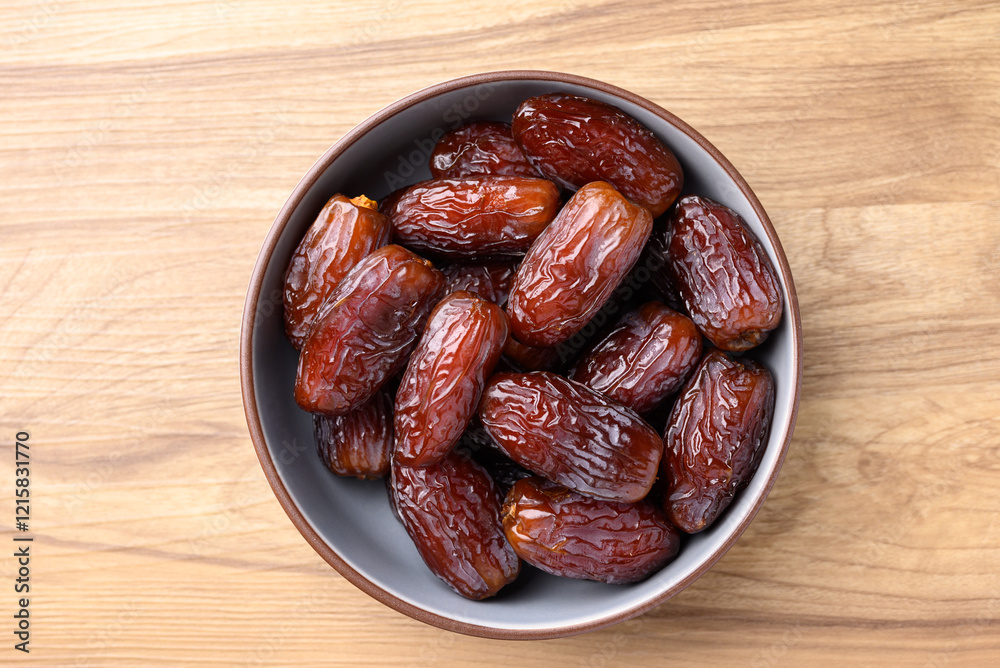 Date palm fruit (MedJool) in bowl on wooden background, Table top view Date palm fruit (MedJool) in bowl on wooden background, Table top view