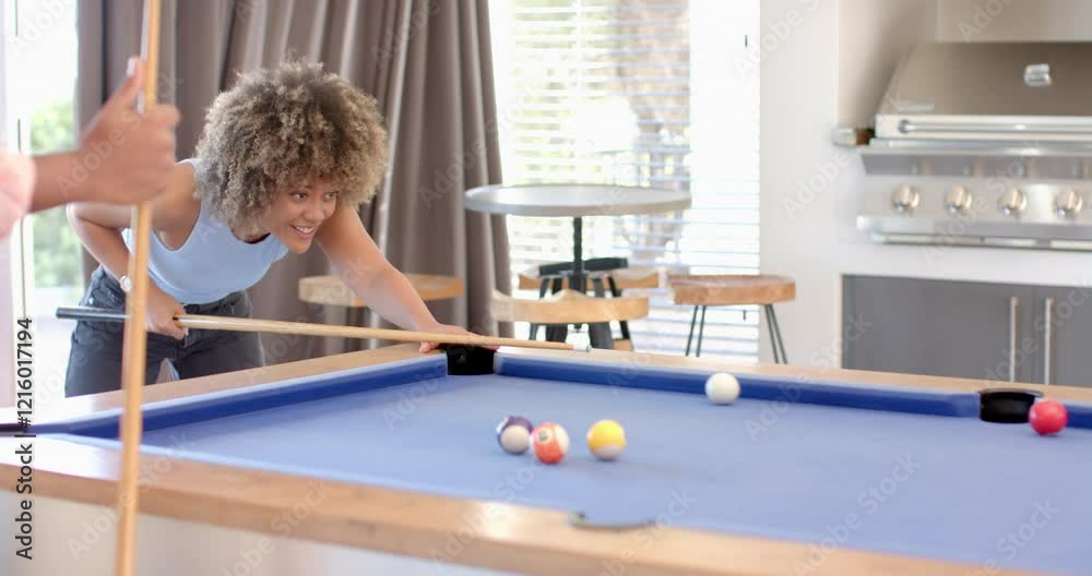 Playing pool, woman aiming cue stick at billiard balls on table with Diverse friends