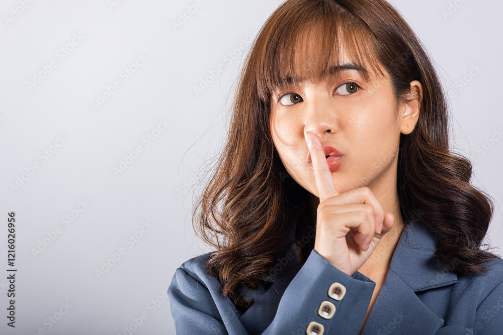 A businesswoman wearing a suit signals silence by placing her finger on her lips in a studio shot on a white background. Copy space available A businesswoman wearing a suit signals silence by placing her finger on her lips in a studio shot on a white background. Copy space available