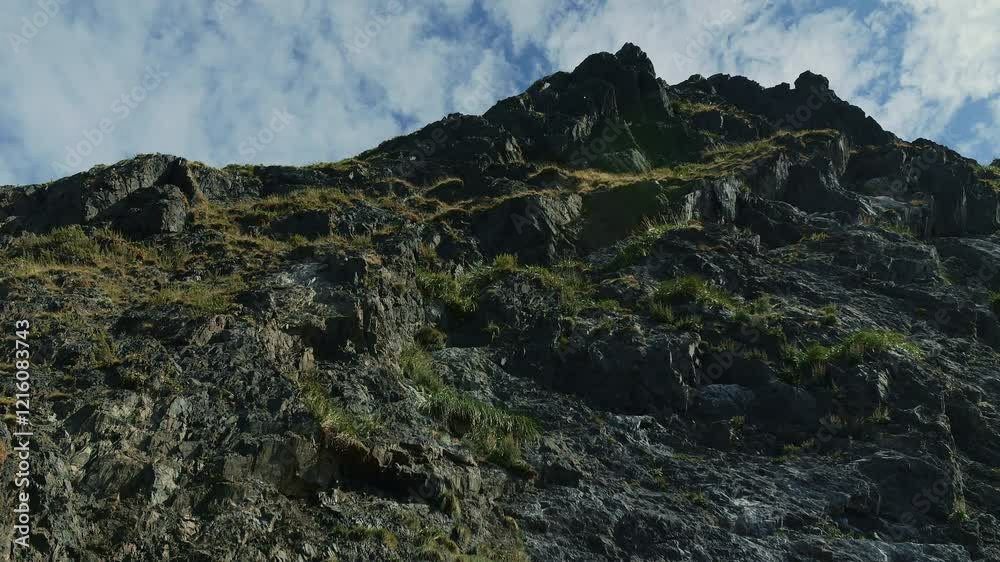 Rugged cliff with grassy patches under blue sky Rugged cliff with grassy patches under blue sky